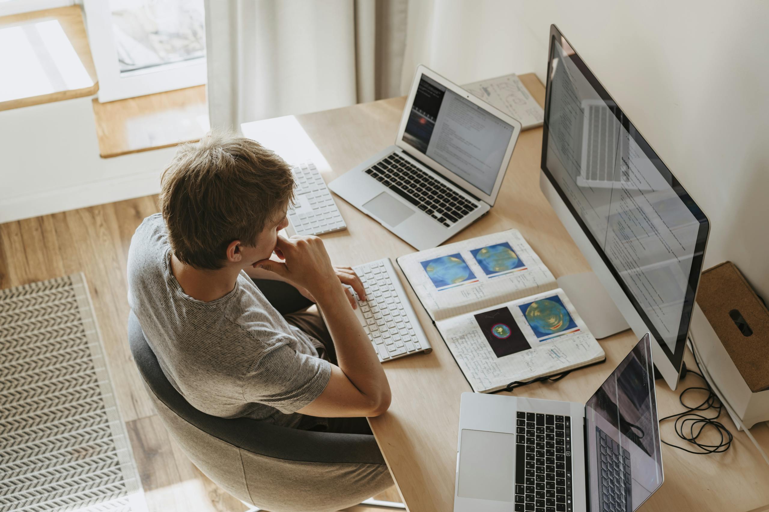 High-Angle Shot of a Boy Sitting on Grey Chair while Using His Laptop Computers